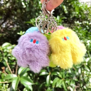 Macro shot of fluffy colorful plush monster keychains with detailed embroidery and metal hooks