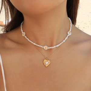 Detail of layered gold necklace with white daisies and heart pendant on a sunny beach