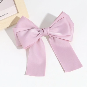Detail of a soft pink satin bow hair clip featuring a smooth glossy silk texture