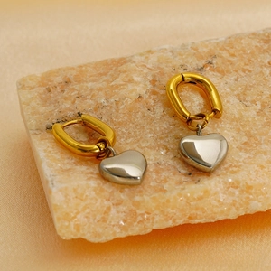 Détail de boucles d'oreilles cœur bicolores or et argent sur un présentoir en pierre