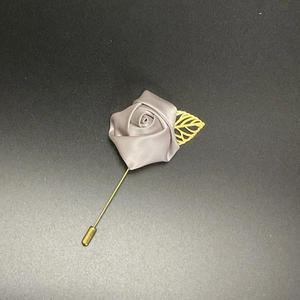Detail of grey satin rose lapel pin with golden leaf and long metal needle fastener