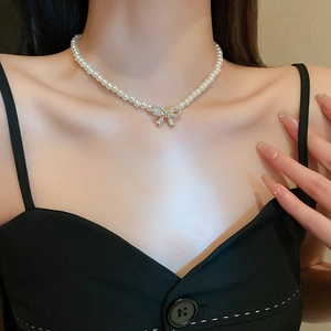 Detail of elegant pearl necklace with gold diamond bow pendant worn by a model