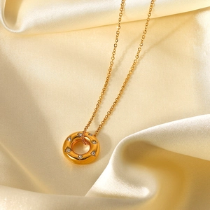 Detailed shot of 18K gold hollow ring pendant with cubic zirconia on beige silk fabric