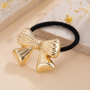 Detailed view of a metallic gold bow hair tie with textured finish on a decorative stone