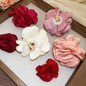 Nahaufnahme handgefertigter Stoffblumen-Ringe in Burgunderrot und Rosa auf Holztablett