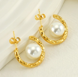 Detailed view of golden hammered C-shaped hoop earrings featuring a large center white pearl