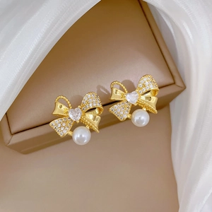Elegant gold bow earrings with pearls and crystals displayed on a jewelry box