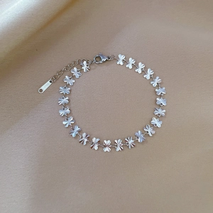 Macro detail of stainless steel clover bracelet with radial texture on champagne silk