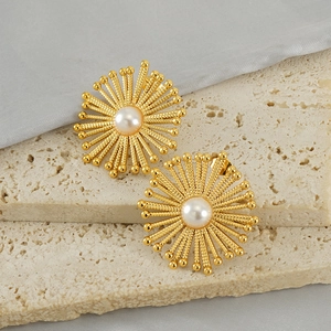 Golden geometric sunflower stud earrings with white pearl center on a stone surface