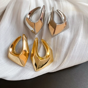 Détail de boucles d'oreilles géométriques dorées et argentées sur tissu blanc