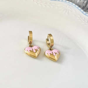 Gros plan de boucles d'oreilles cœur dorées avec émail rose sur une assiette en céramique