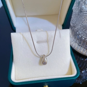Macro shot of silver teardrop pendant and snake chain on beige velvet jewelry box