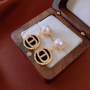 Macro view of gold plated pearl earrings with zircon inlay and CD letter pendant detail