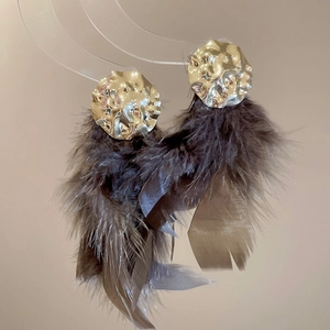 Close-up of bohemian earrings with golden hammered metal discs and brown feathers