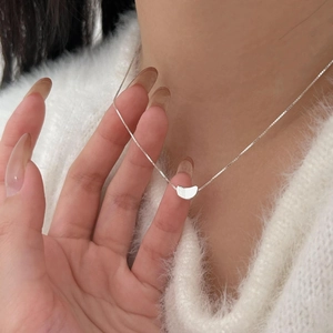 Close-up of minimalist silver curved pendant necklace worn on a white knit sweater