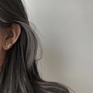 Detail view of a matte gold butterfly stud earring worn on a model's ear