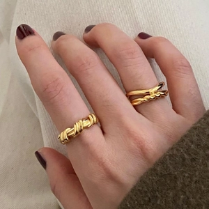 Detail view of woven and double-layered gold rings worn by a model with red nails