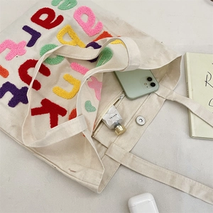 Detail of canvas tote bag featuring chenille letter embroidery and magnetic buckle