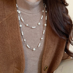 Detail of layered long pearl necklace with silver chain on elegant brown coat