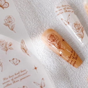 Rose gold floral nail stickers with butterfly and feather designs on white background