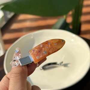 Close-up of amber acetate hair clip with colorful rhinestones on a white plate