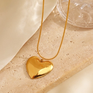 Golden heart pendant necklace with thin snake chain displayed on beige stone and silk