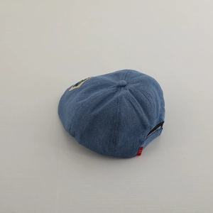 Dettaglio del berretto in denim blu scuro per bambini con ricamo e etichetta rossa
