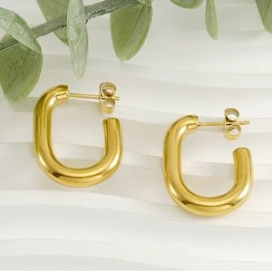 Detailed view of gold U-shaped earrings on a white textured background with green leaves