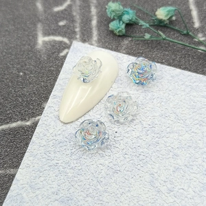 Macro shot of iridescent camellia 3D nail charms on a white nail tip and textured paper