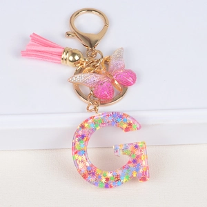 Detail of letter G keychain with pink tassel, resin butterfly and colorful star sequins