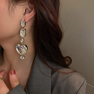 Detailed view of oversized rhinestone heart earrings worn with a chic grey suit