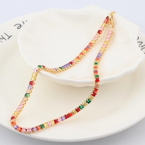 Macro detail of rainbow zircon stones set in a gold chain on a white ceramic plate