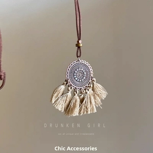 Détail du pendentif bohème rond en métal gravé avec pompons crème et cordon vintage