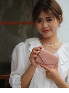 Slim pink pebble grain leather wallet with envelope flap and button held by a hand