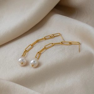 Macro shot of 18K gold plated chain earrings with pearls on beige silk fabric