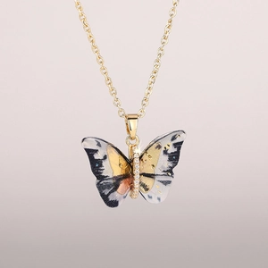 Detailed close-up of a golden butterfly pendant with black and white ink texture and zircons