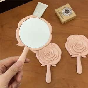 Tragbarer handgehaltener Kosmetikspiegel in Rosenform aus rosa Kunststoff auf Holz