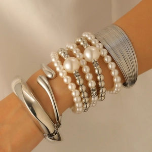Detail of layered silver metal bracelets and cream pearl beaded set on model wrist