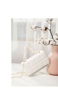Detail of white quilted crossbody bag with golden chain and resin handle decor