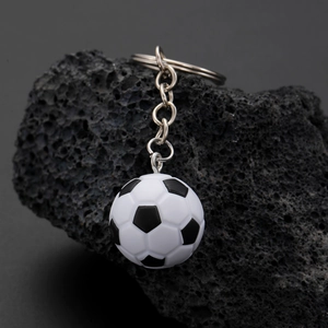 Close-up of black and white resin soccer ball keychain hanging against a dark volcanic stone