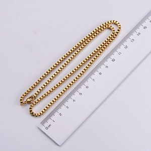 Macro shot of a 18k gold stainless steel box chain measured by a ruler on white background