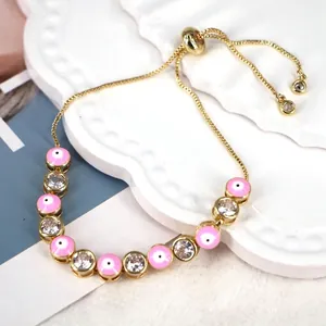 Detail of pink enamel evil eye charm and clear zircon stones on gold adjustable bracelet