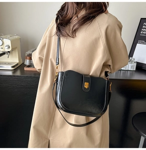 Glossy black saddle bag with gold buckle worn by a model in a beige trench coat