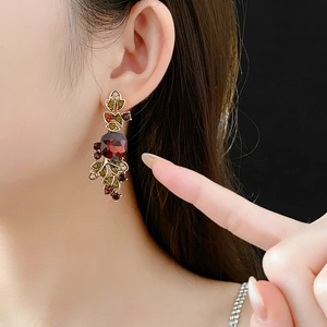 Close-up of vintage gold leaf earrings with garnet red stones and colorful crystals