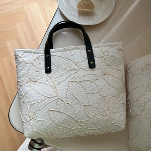 Detail shot of leaf embroidery pattern on cream tote bag with black leather handle