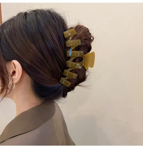 Detail of a large olive green acrylic hair claw clip holding a full bun hairstyle