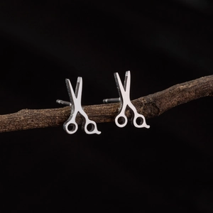 Minimalist silver scissors stud earrings in stainless steel on a dark wood stand