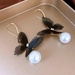 Close-up of golden butterfly earrings with black lace wings, rhinestones, and large pearls