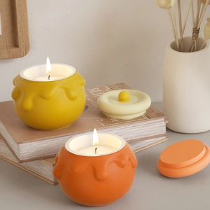 Dettaglio di candele accese a forma di vasetto di miele in ceramica gialla e arancione