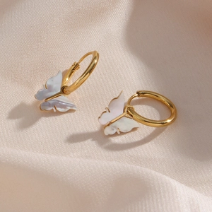 Macro shot of gold hoop earrings with white shell butterfly charms on beige silk fabric